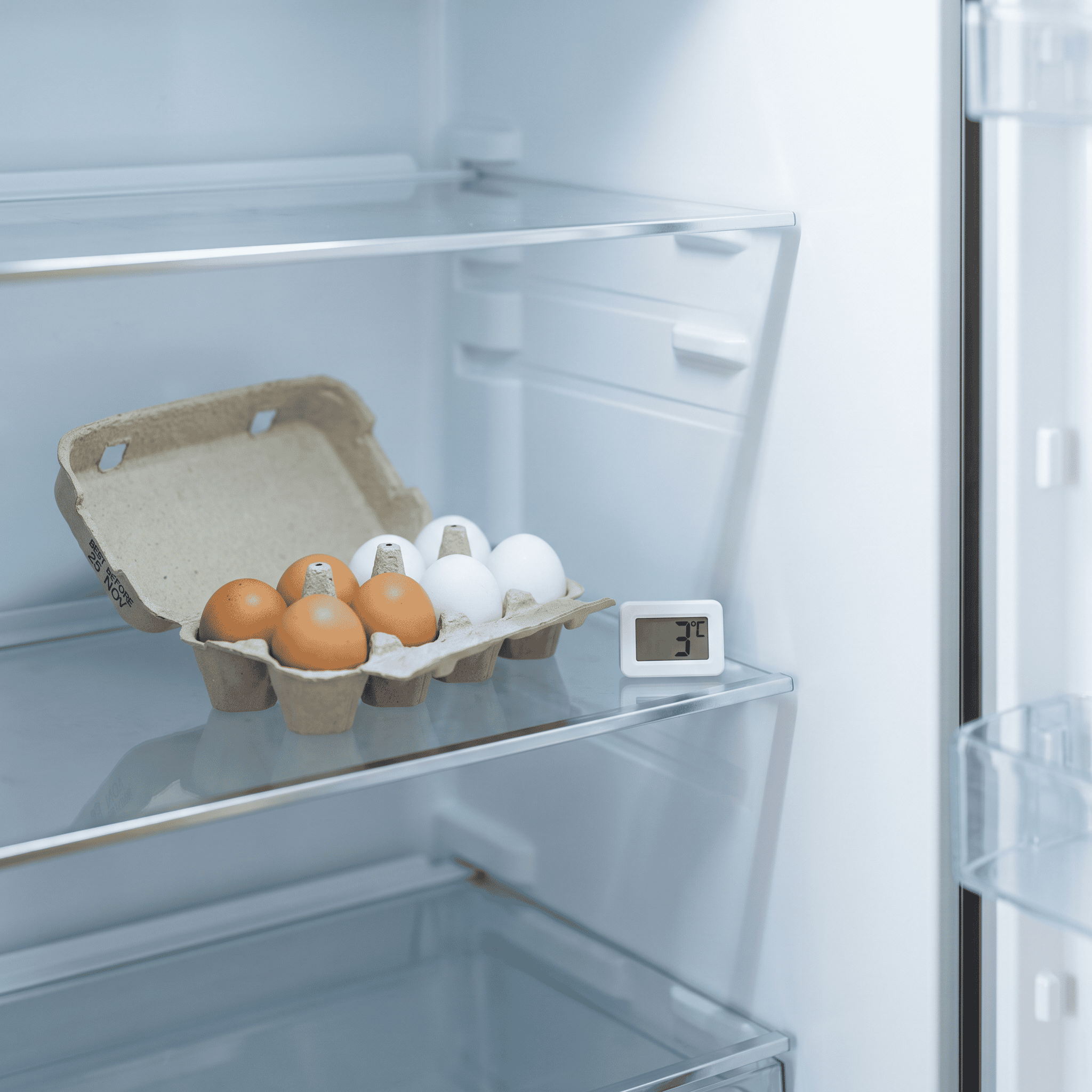 How Long Do Eggs Last in the Fridge? 1 Carton of eggs on a fridge shelf next to a thermometer reading 3 degrees Celsius